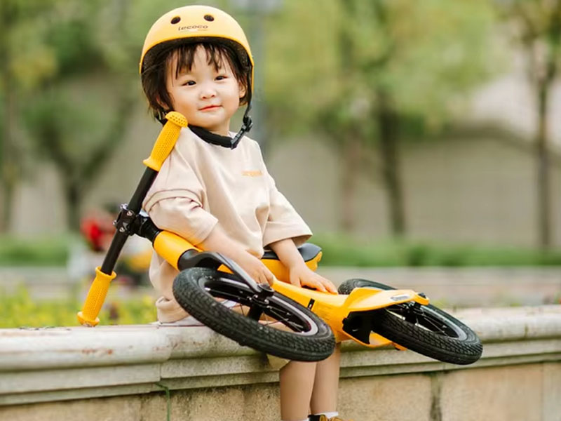 A young girl carries her lightweight balance bike