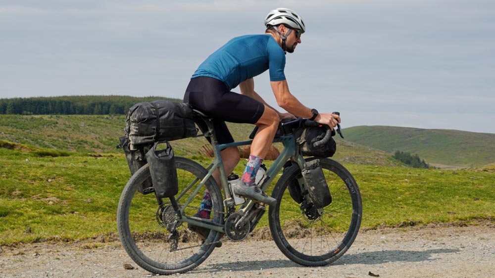 Rider managing a disorganized bikepacking setup with overloaded gear